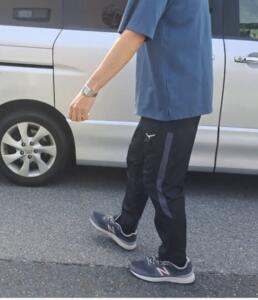 Person walking beside a silver minivan, wearing a blue shirt, black jogger pants with a blue stripe, and navy New Balance sneakers